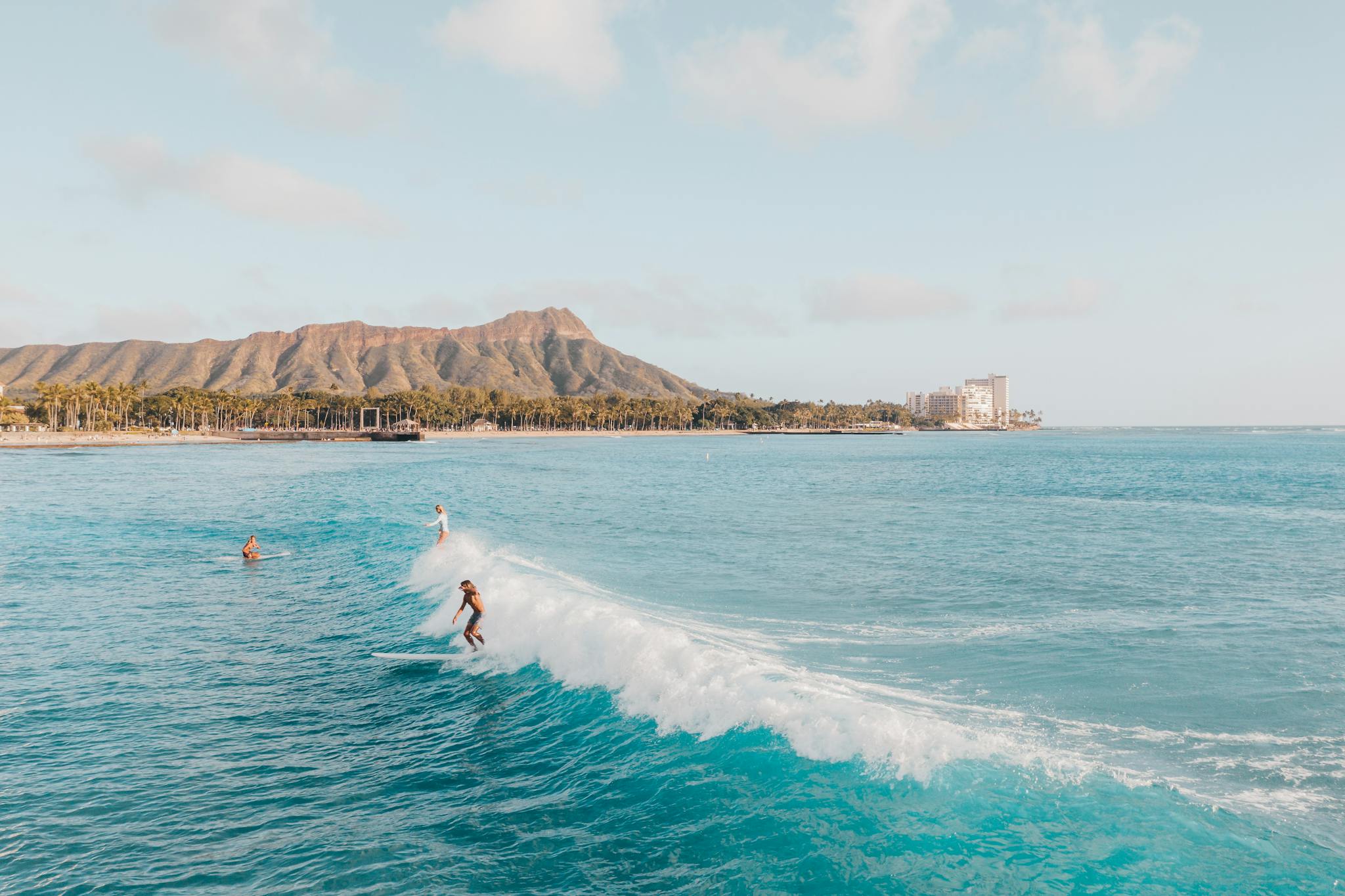 Surfers enjoy waves at Diamond Head, Hawaii, with scenic ocean and mountain views.