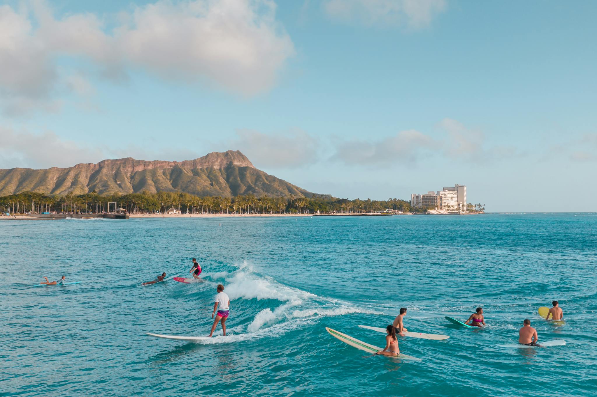 Surfers ride waves at Waikiki Beach with Diamond Head backdrop. Experience Hawaiian surf life in this stunning photo.